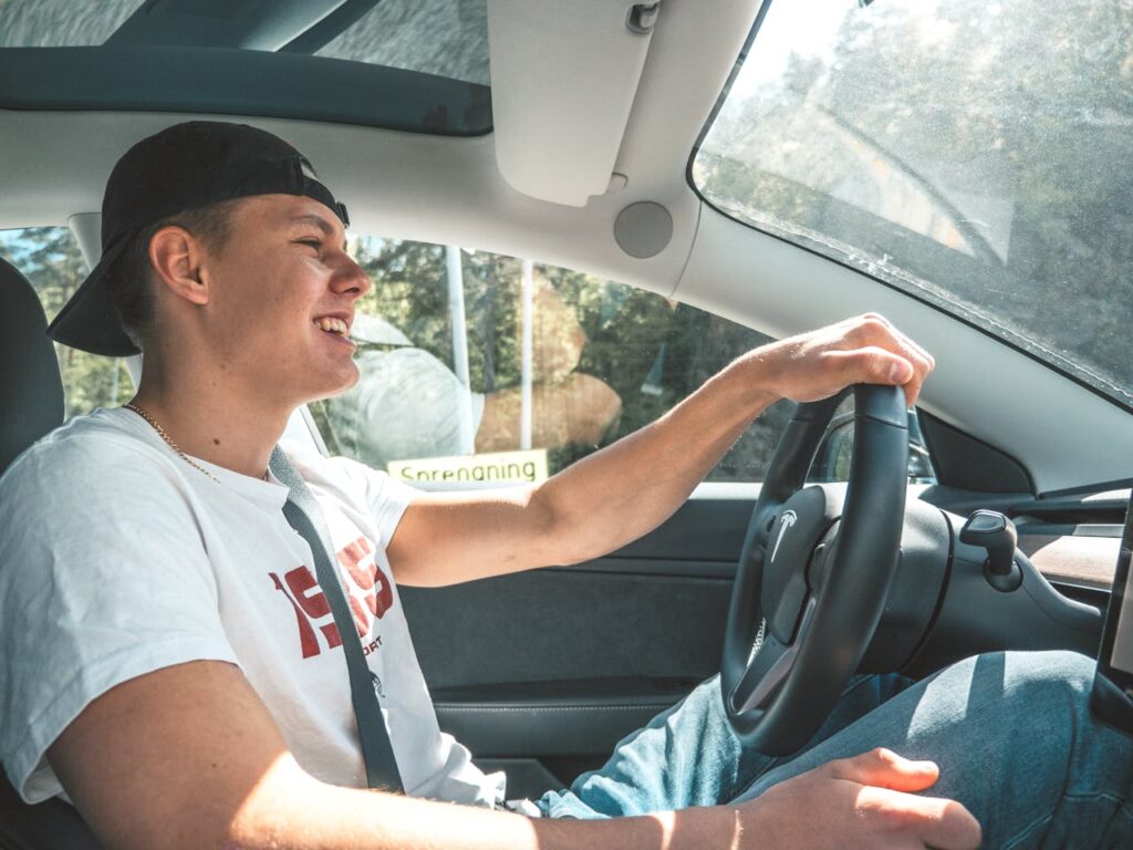 Young man happily driving a modern car in Kristiansand, showcasing a joyful travel experience.